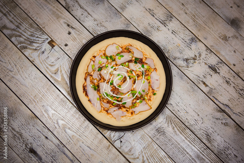 Round pizza dough is in the pan. The process of cooking pizza, stacking ingredients on the dough.