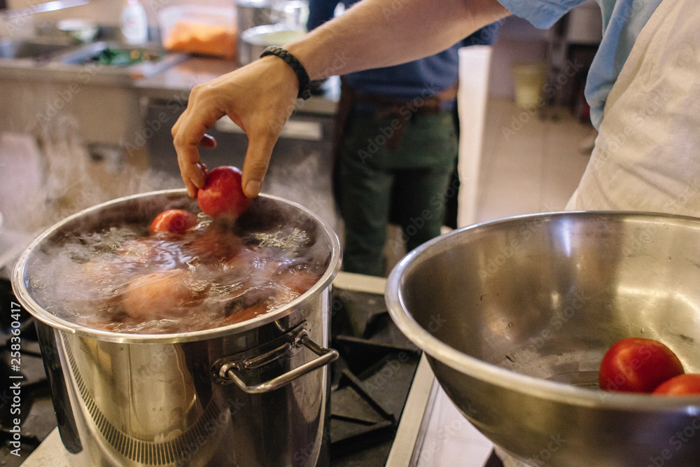 A man puts a tomato in a pot of boiling water. The process of making