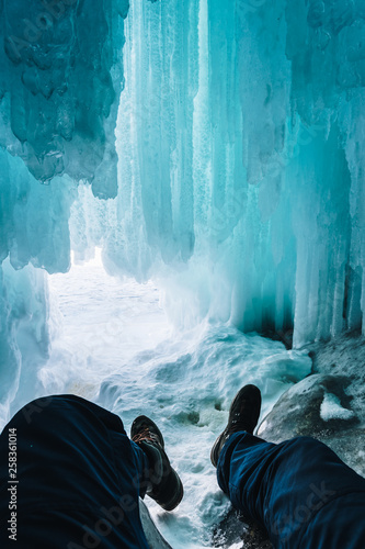 A man sits in an ice cave with hanging icicles. Baikal, Russia. photo