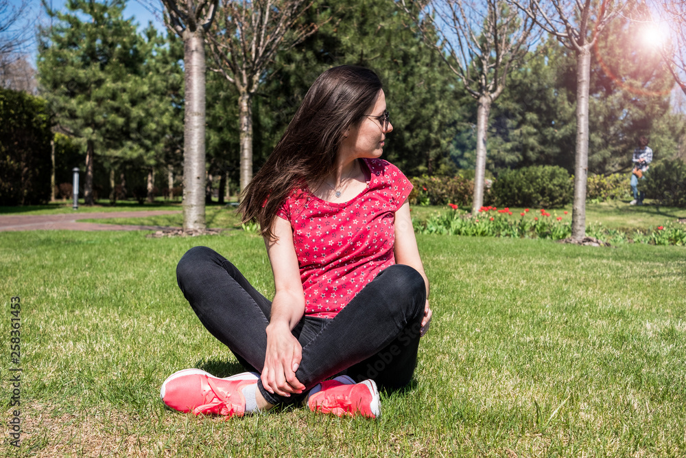 Cute long-haired girl sitting on the green lawn and looks to the side Cute long-haired girl sitting on the green lawn and looks to the side
