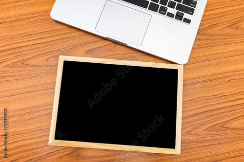 Top view. Small blackboard and laptop put on wood background with texture. Free space on the blackboard for text input.