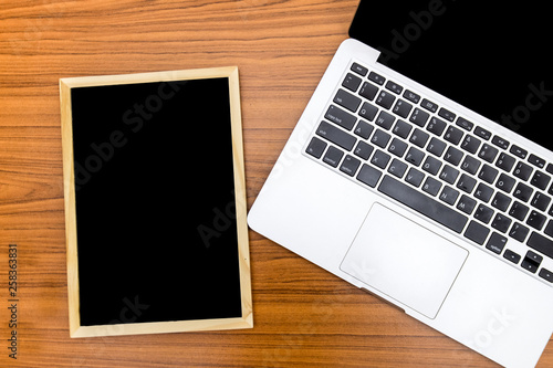 Top view. Small blackboard and laptop put on wood background with texture. Free space on the blackboard for text input.