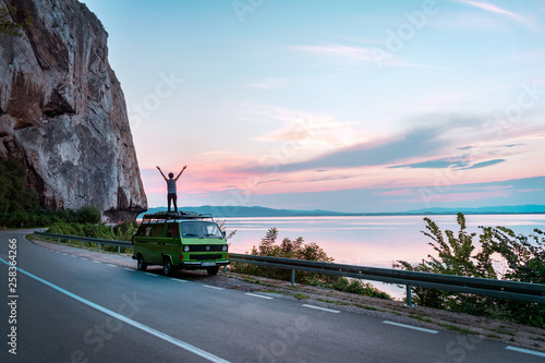 Obraz na plátně Young girl standing on top of vintage classic camper van with hands wide open