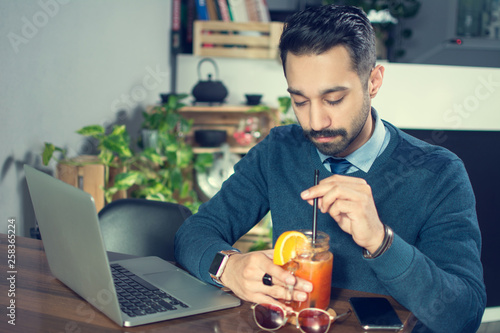 Young businessman working with laptop and drinking cocktail at office