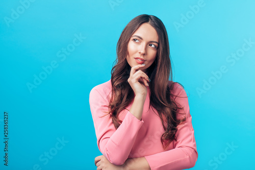 Portrait of thoughtful wondering woman looking sideways isolated over blue background