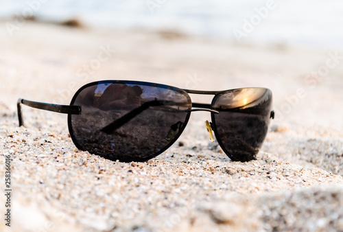 sunglasses on sand with reflection of sunset at sea and photographer