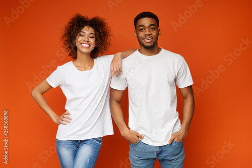 Cheerful black guy and girl posing on orange studio background