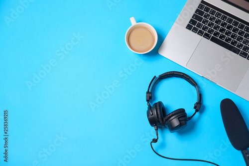Music or podcast background with headphones, microphone, coffee and laptop on blue table, flat lay. Top view, flat lay photo