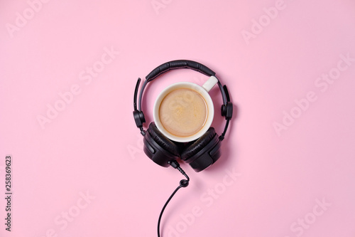 Music or podcast background with headphones and cup of coffee on pink table, flat lay. Top view, flat lay