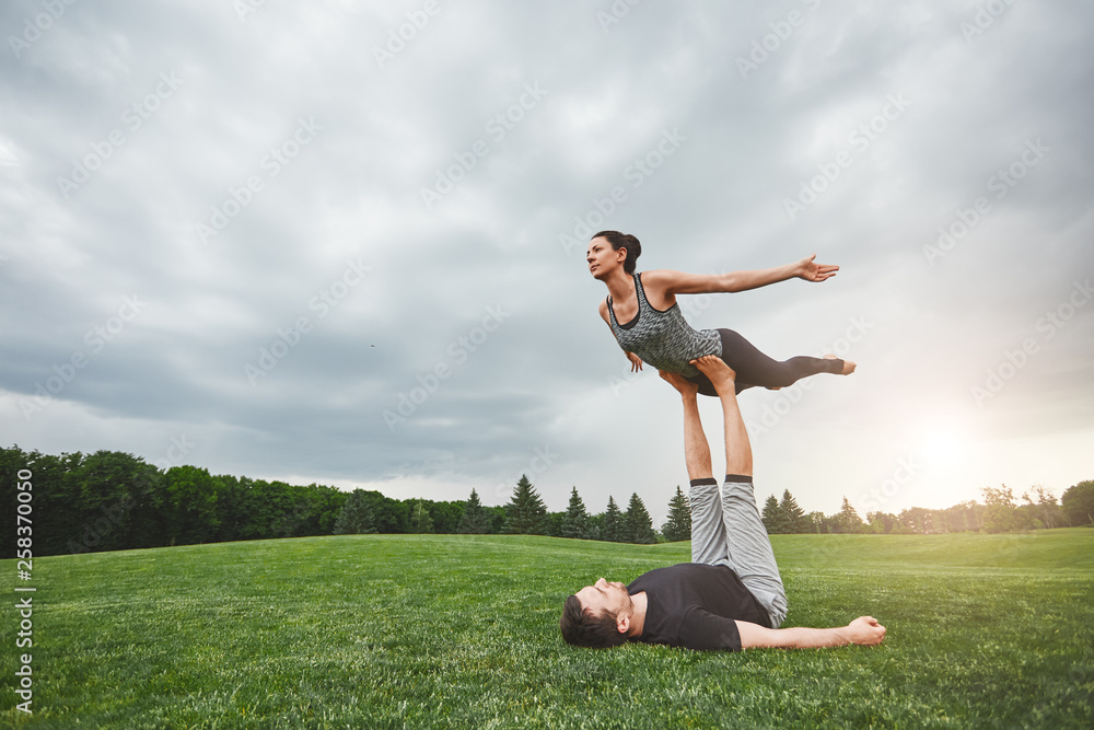 Healthy lifestyle. Strong man lying on grass and balancing woman on his feet. Young couple practising acro yoga in nature. Healthy lifestyle. Strong man lying on grass and balancing woman on his feet. Young couple practising acro yoga in nature.