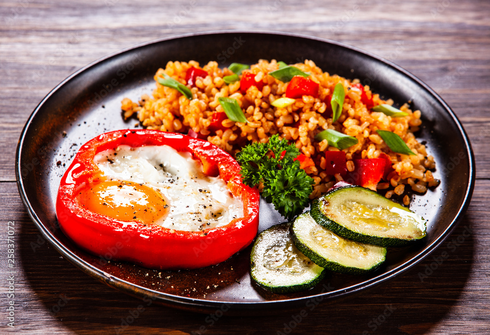 Fried egg, groats and vegetables on wooden table