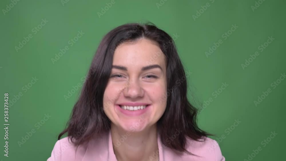 Young brunette businesswoman in pink jacket blowing a kiss happily into camera on green background. Young brunette businesswoman in pink jacket blowing a kiss happily into camera on green background.