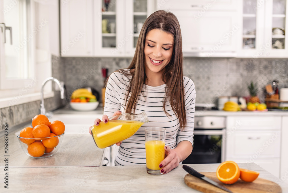 Close up portrait of a woman pouring orange juice in the glass while sitting at the kitchen