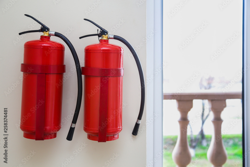 Obraz premium 2 fire extinguishers hang on a light wall near windows