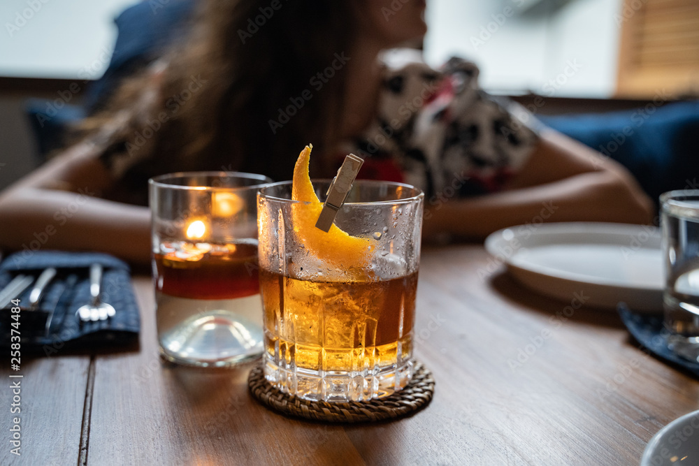 Old fashioned cocktail served in a whiskey glass at the restaurant. Woman in soft focus in the back ground. Copy space Old fashioned cocktail served in a whiskey glass at the restaurant. Woman in soft focus in the back ground. Copy space