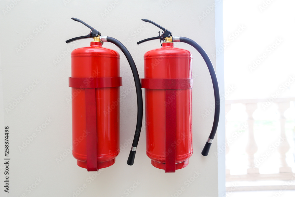 2 fire extinguishers hang on a light wall near windows 2 fire extinguishers hang on a light wall near windows