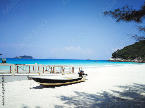 A boat is located by the beach in a tropical island beach with ombre sea in the background. © ellinnur