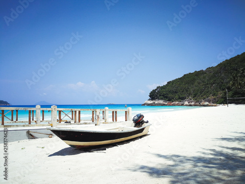 A boat is located by the beach in a tropical island beach with ombre sea in the background.