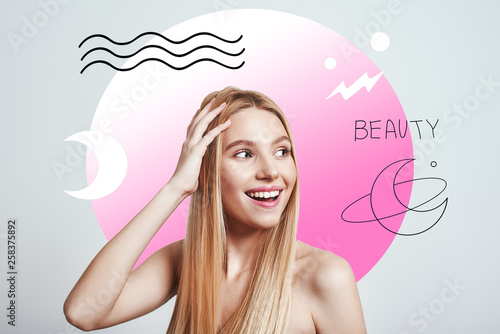 Feeling beautiful. Attractive young woman with naked shoulders touching her hair and smiling while standing against abstract creative background with hand drawn illustrations.