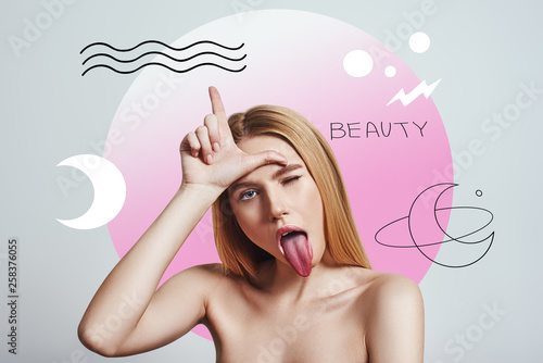 Crazy beauty. Funny blonde girl is making a face, gesturing and sticking out tongue while standing against abstract pink circle and hand drawn illustrations.