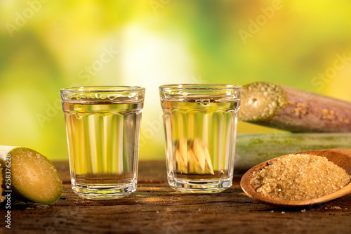 two shot glasses of Brazilian gold  cachaca with sugar and sugarcane isolated on rustic wooden background photo