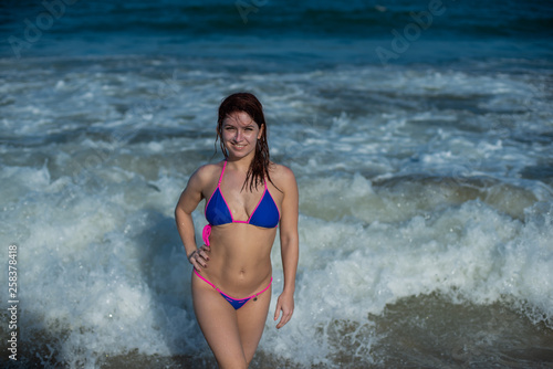 beautiful young woman in a seductive bikini comes out of the sea with high waves. Big waves in the ocean