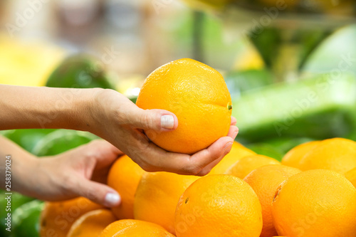 Woman's hand choosing orange fruit in supermarket