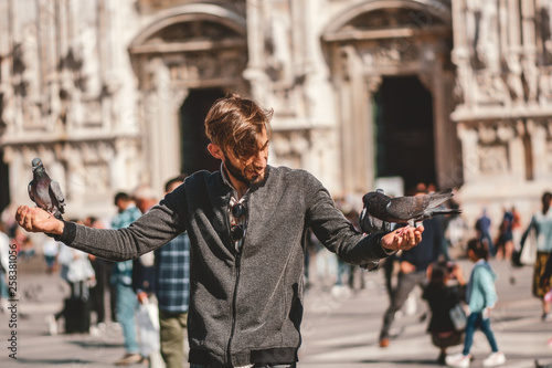 Foto Young man posing with pigeons in the milanese street with ancient church Duomo di Milano on background
