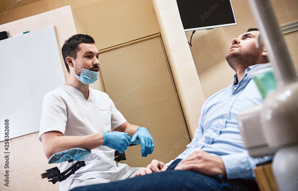Obraz premium Dentistry with a personal touch. Dentist in mask and latex gloves sitting near his patient in dental clinic