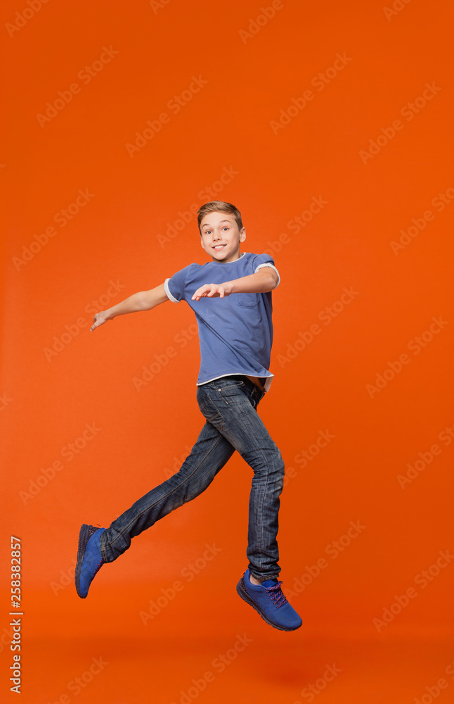 Cute boy dancing, jumping in air on orange backgrouns