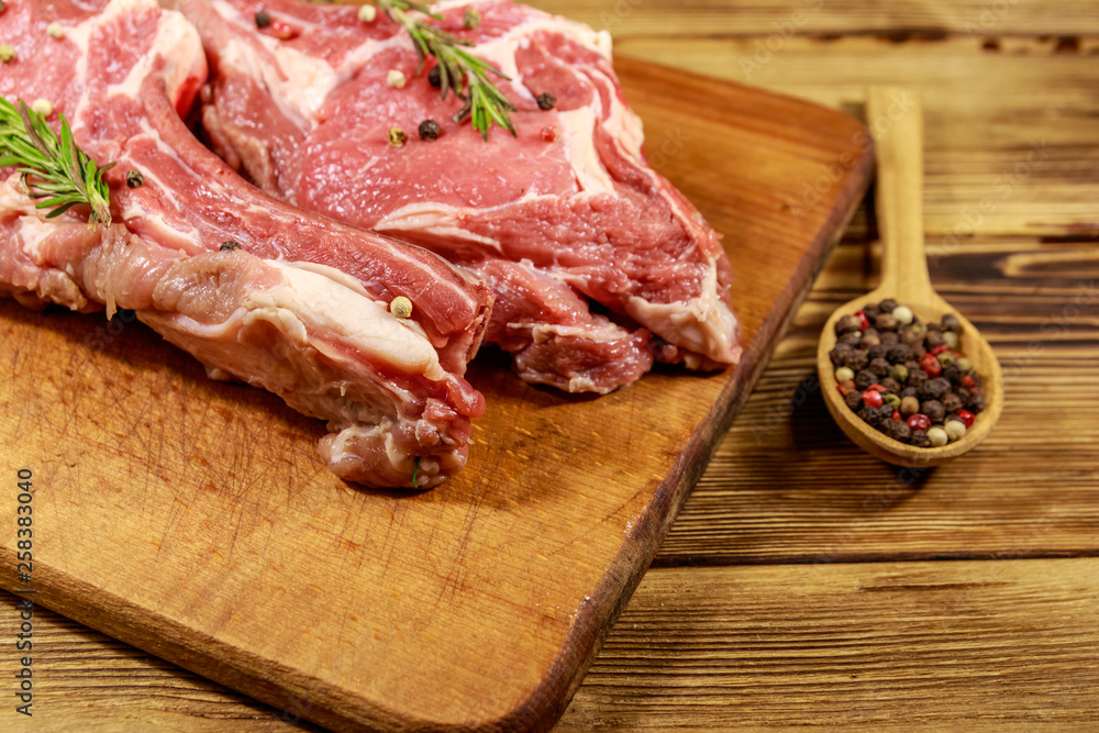 Raw fresh beef rib eye steaks on bone with spices and rosemary on wooden table Raw fresh beef rib eye steaks on bone with spices and rosemary on wooden table
