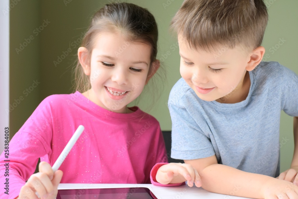 White caucasian toddler boy and beautiful girl drawing together on tablet screen. Portrait of a happiness little brother and sister. Children play a computer game on the tablet White caucasian toddler boy and beautiful girl drawing together on tablet screen. Portrait of a happiness little brother and sister. Children play a computer game on the tablet