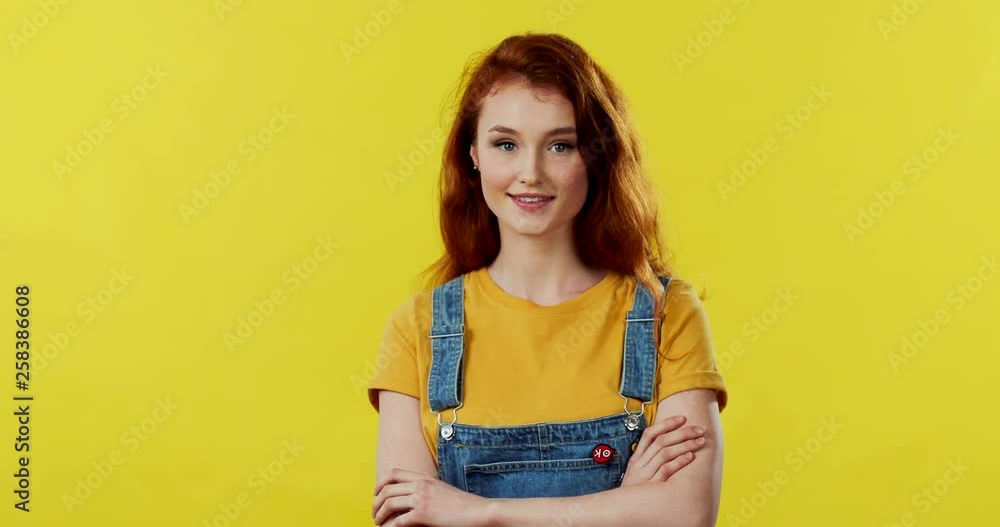 Portrait shot of the pretty Caucasian young red haired woman being a coquette and smiling to the camera on the yellow background. Portrait shot of the pretty Caucasian young red haired woman being a coquette and smiling to the camera on the yellow background.