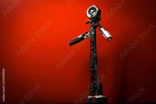 Small welded figurine of scrap metal and screw bolt as a head with wondering attitude against a red background