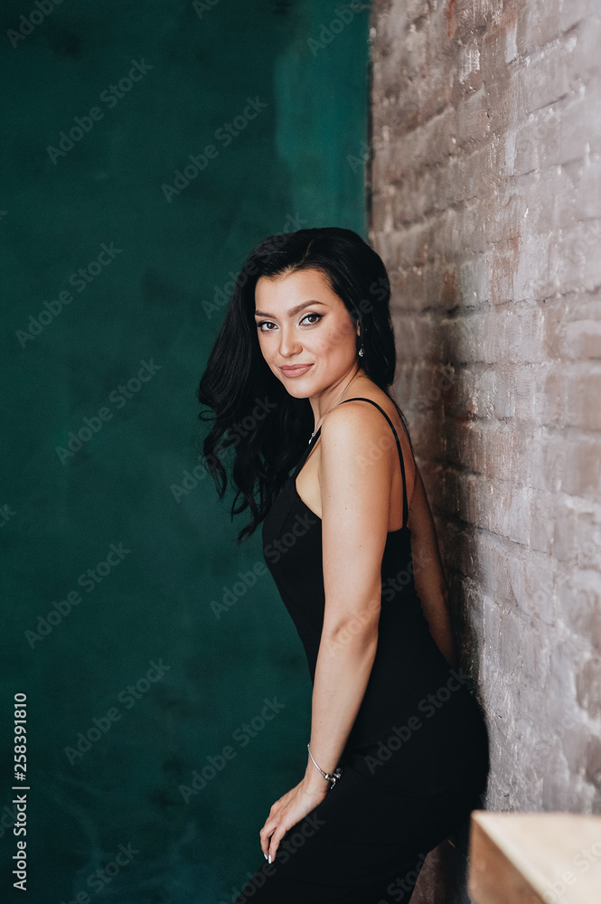 Beautiful girl in a black tight-fitting dress and heels. Black long wavy hair. Eastern appearance. Beautiful cut eyes. Brown sofa and green wall. A dark room. Sexy and stingy brunette. Portrait. Beautiful girl in a black tight-fitting dress and heels. Black long wavy hair. Eastern appearance. Beautiful cut eyes. Brown sofa and green wall. A dark room. Sexy and stingy brunette. Portrait.