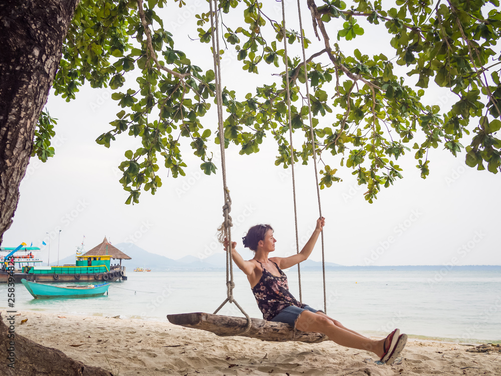 Obraz premium Caucasian woman is swinging on a wooden swing at the beach