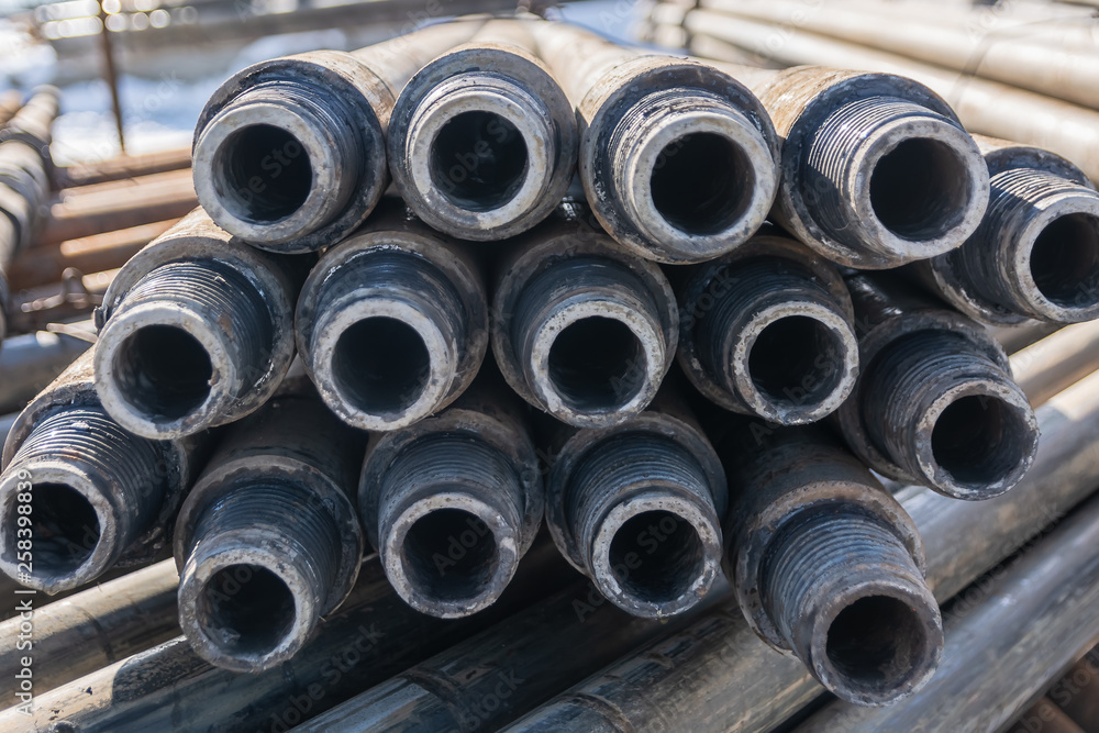 Drill pipes for drilling oil and gas wells are located horizontally on the rack. In the foreground is a threaded pipe joint. In the background is a blurred image of the other pipes. Drill pipes for drilling oil and gas wells are located horizontally on the rack. In the foreground is a threaded pipe joint. In the background is a blurred image of the other pipes.