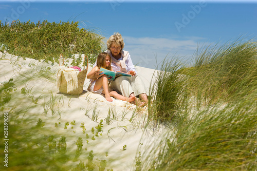 Grand mother and grand daughter reading on the beach