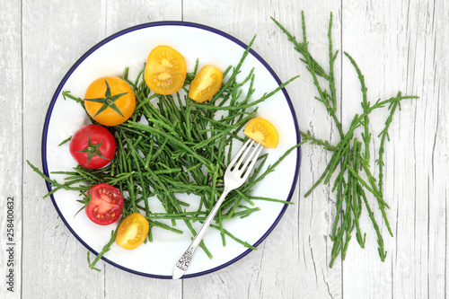 Samphire health food sea vegetable with yellow and red tomatoes on a metal plate with old silver fork, high in antioxidants, fucoidans, dietary fiber and calcium. Salicornia europaea