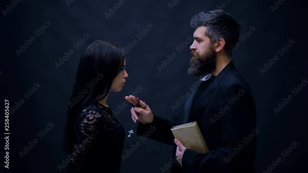 Religious priest in religion concept against dark background. Priest and parishioner pray on a black background. Religion is an opium for the people. Religious priest in religion concept against dark background. Priest and parishioner pray on a black background. Religion is an opium for the people.