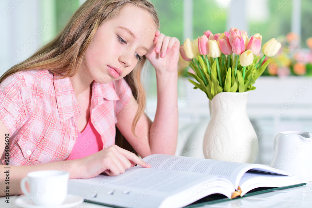 Cute schoolgirl sitting at table and reading Cute schoolgirl sitting at table and reading