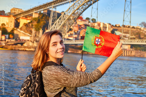 Young woman tourist with portuguese flag enjoying beautiful landscape view on the old town with river and famous iron bridge Dom Luiz during the sunset in Porto city, Portugal © bondvit