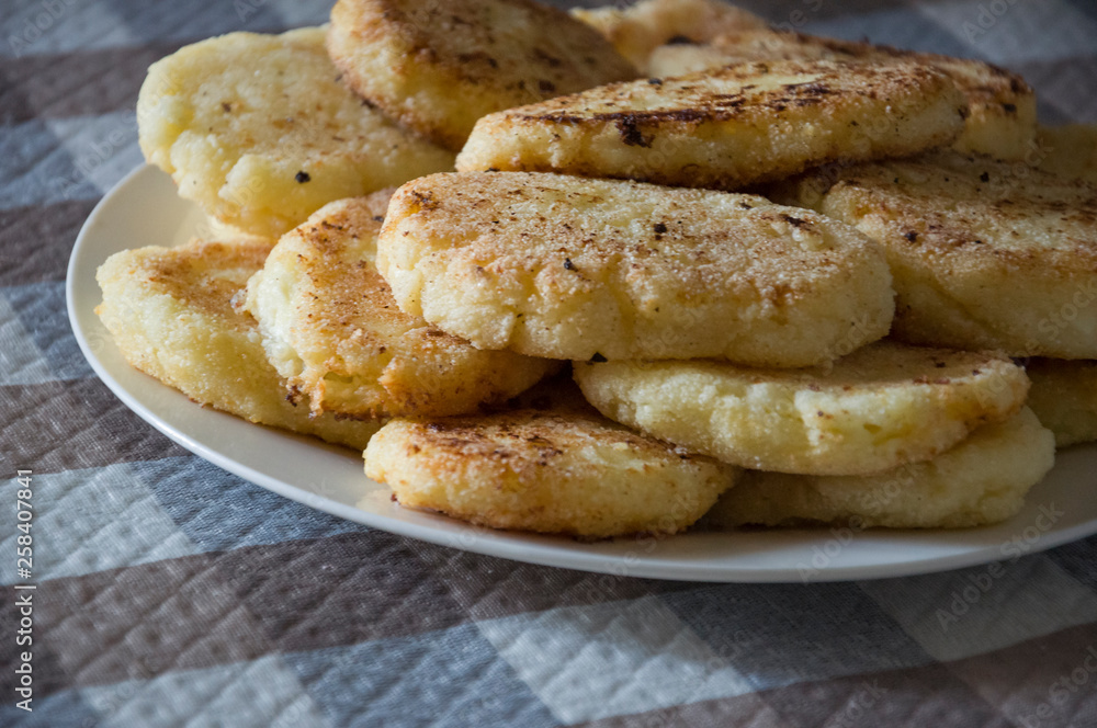 Hot tasty baked cheese pancakes in the plate standing on the checkered tablecloth. Breakfast Hot tasty baked cheese pancakes in the plate standing on the checkered tablecloth. Breakfast