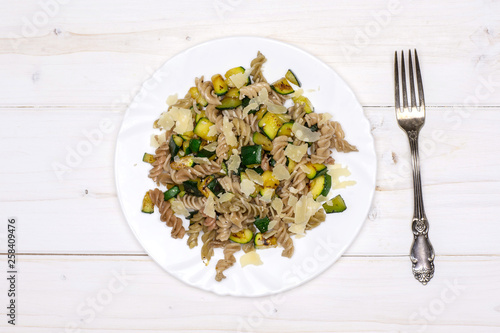 Ready to eat. recipe step by step fusilli pasta with zucchini on white porcelain plate with a fork flatlay on white wood photo