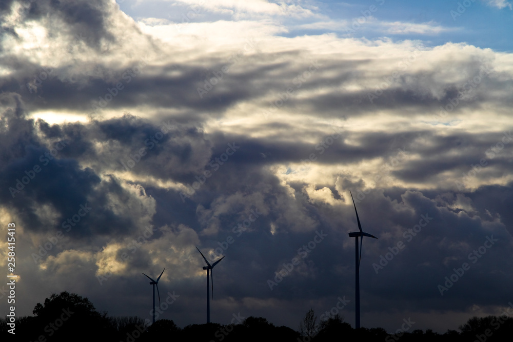 dramatic sky behind a wind farm with light peaking though the clouds dramatic sky behind a wind farm with light peaking though the clouds