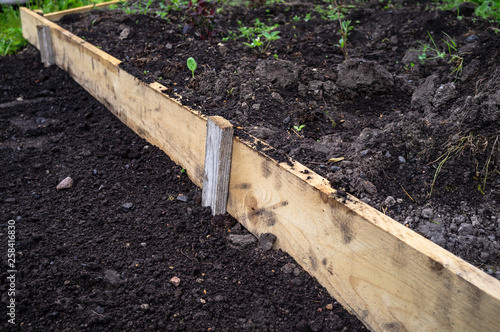 Garden bed fenced with wooden plank, in the countryside garden, on a spring day. Soil preparation for planting vegetables.