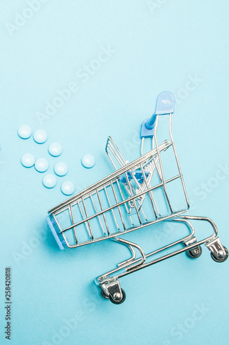 Pills and Shopping trolley on blue background. Creative idea for health care cost, drugstore, health insurance and pharmaceutical company business concept. Copy space