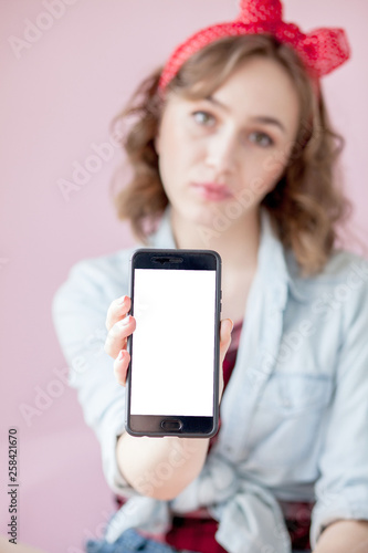 Beautiful young woman with pin-up make-up and hairstyle over pink background with mobile phone with copy space