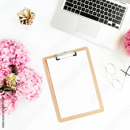 Stylized women's desk. Workspace with clipboard, laptop, bouquet hydrangea, accessories on white background. Flat lay. Top view.