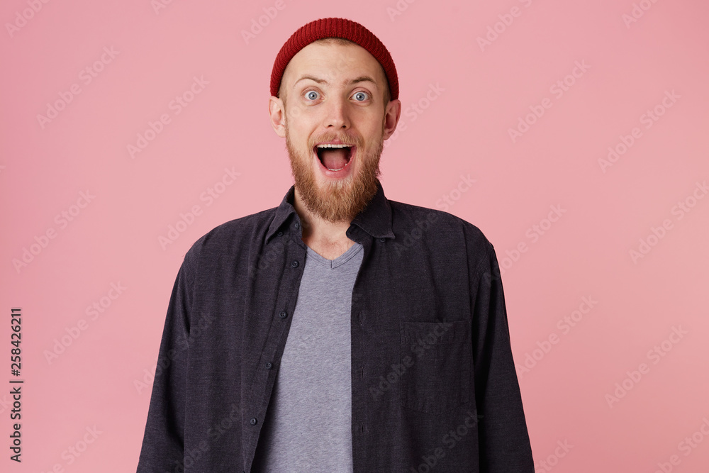 Photo of amazed happy bearded man man in blank shirt and t-shirt, with red hat, screaming in surprise, popping his eyes in surprisement, looking glad, looking at the camera over pink background . Photo of amazed happy bearded man man in blank shirt and t-shirt, with red hat, screaming in surprise, popping his eyes in surprisement, looking glad, looking at the camera over pink background .